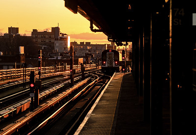 A subway train pulling into an elevated station at sunrise. 